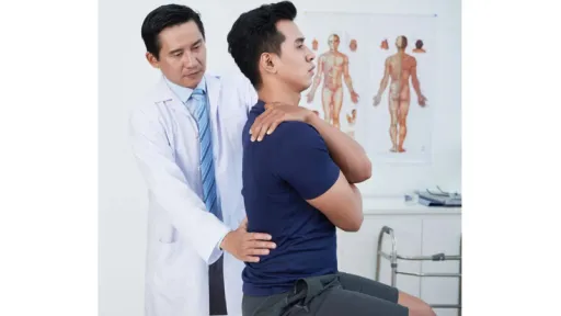 patient sitting on treatment table with arm over shoulder, doctor palpating lower back