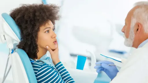 woman at the dentist, explaining jaw pain with her hand on her jaw