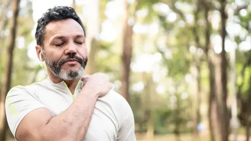 man in the forest with hand on shoulder, signifying pain