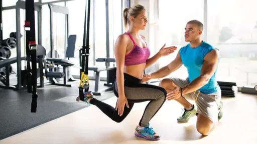 woman in athletic wear lunging with one leg up, trainer next to her