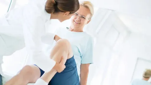 older woman sitting on table, doctor manipulating her knee